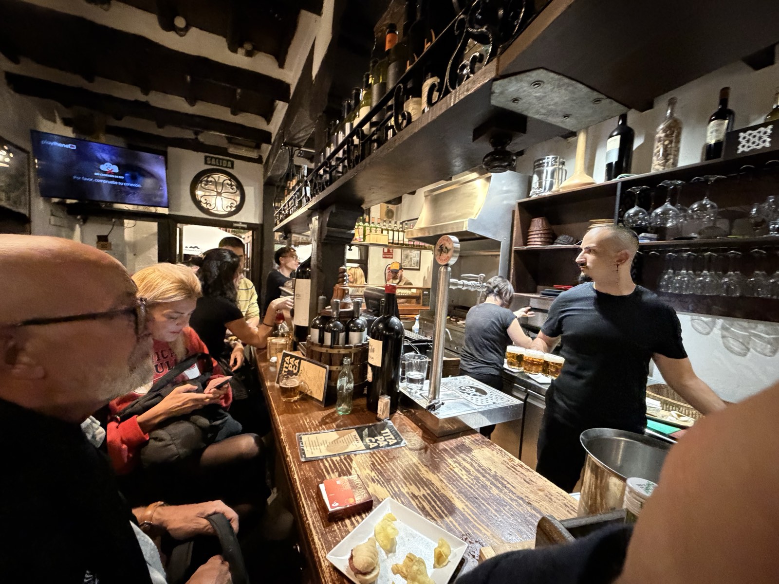 La barra de Taberna Tita Paca: los grifos, el vino y la parrilla al fondo